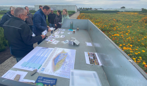 Boomkwekers onderzoeken buiten op een bedrijf welke mogelijkheden er zijn op hun bedrijven, aan de hand van allerlei informatiemateriaal dat op tafel ligt.